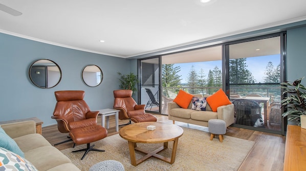 A modern living room with leather chairs, a round wooden coffee table, and a sofa with orange cushions.