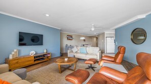 A living room with a TV, wooden entertainment unit, leather sofas, a coffee table, and a ceiling fan.