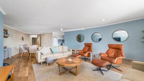 A modern living room with a sofa, two leather armchairs, a coffee table, and a dining area with a table and chairs.