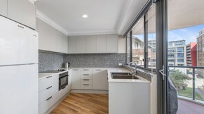 A modern kitchen with white cabinets, a black and white backsplash, and a large window offering a view of the city.