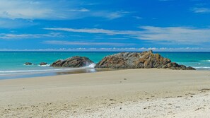 A beach with clear skies, calm waters, and rocky formations.