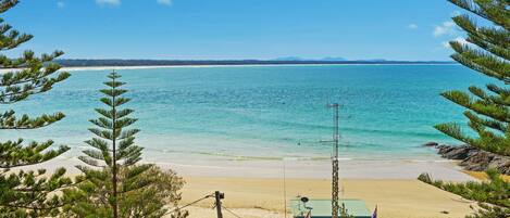 Une plage avec une eau turquoise et limpide, un rivage sablonneux et un petit bâtiment surmonté d’un toit vert.