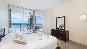 Een slaapkamer met een bed, een dressoir, een spiegel en een balkon met uitzicht op zee.