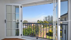 Una habitación con un amplio ventanal corredero que da a un balcón con vistas a una zona residencial y zonas verdes.