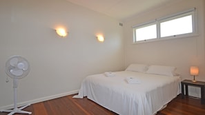 Un dormitorio con una cama, una mesita de noche, una lámpara, un ventilador de pared y dos apliques.