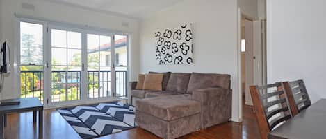 Sala de estar com sofá cinza, tapete estampado e canto de jantar com mesa e cadeiras de madeira.
