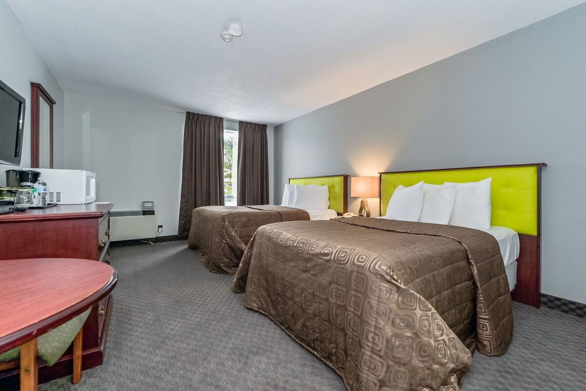 A hotel room with two beds, a desk with a chair, a microwave, and a window with curtains.