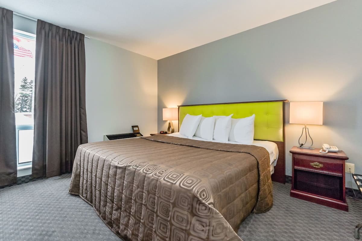 A hotel room with a large bed, two bedside tables, a nightstand, and a window with curtains.