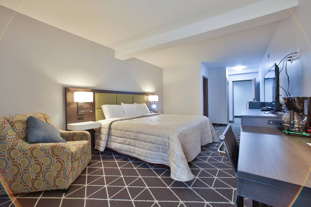 A hotel room with a bed, a desk, a chair, and a kitchenette.