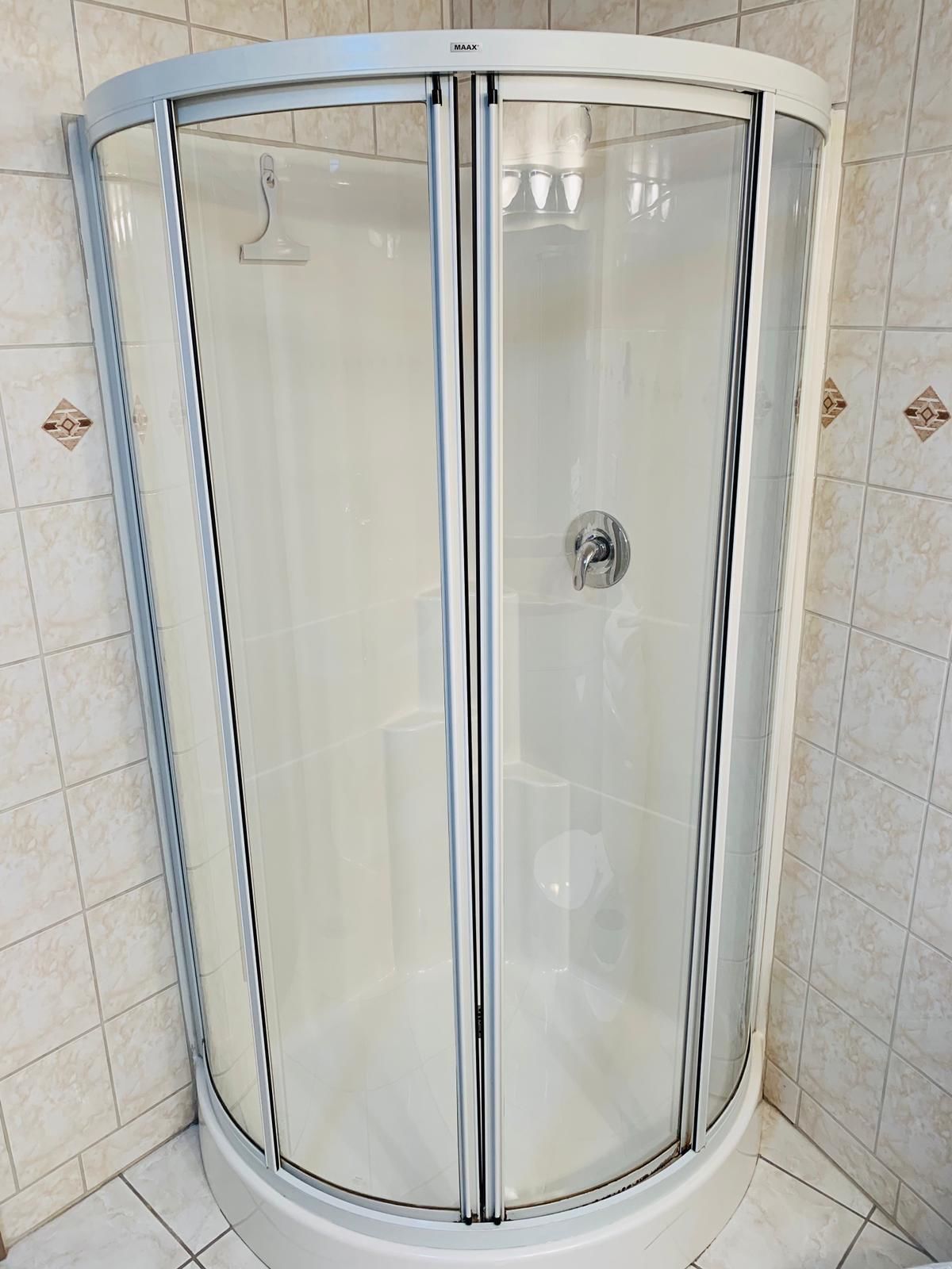 Une cabine de douche fermée par des parois en verre, dotée d’un cadre en chrome et d’une molette de commande fixée au mur.