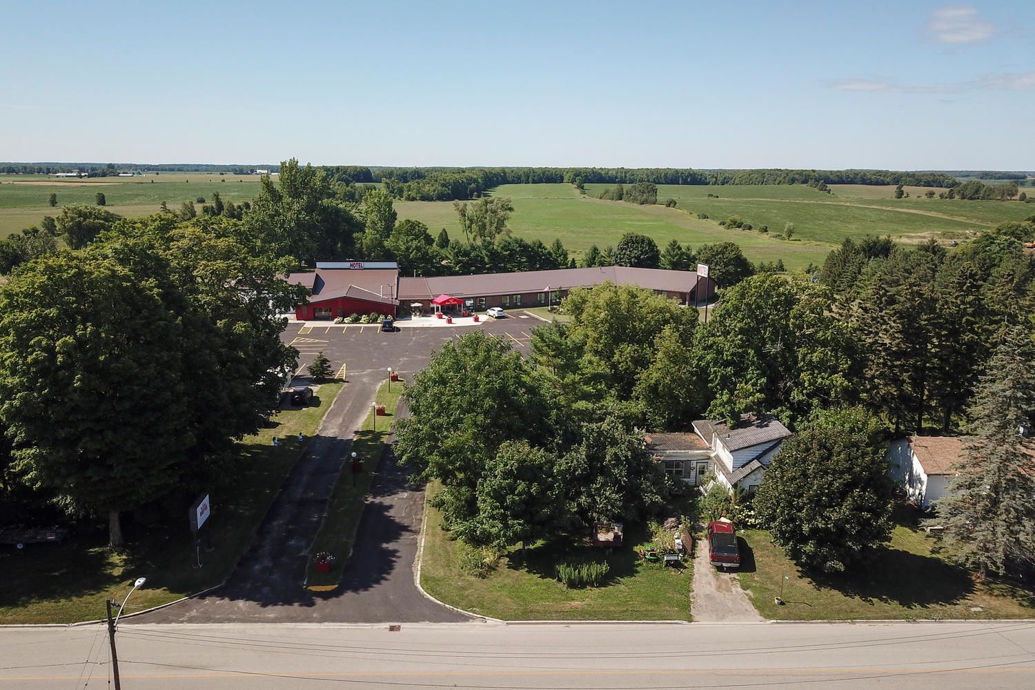A motel with a parking lot, surrounded by trees and fields.