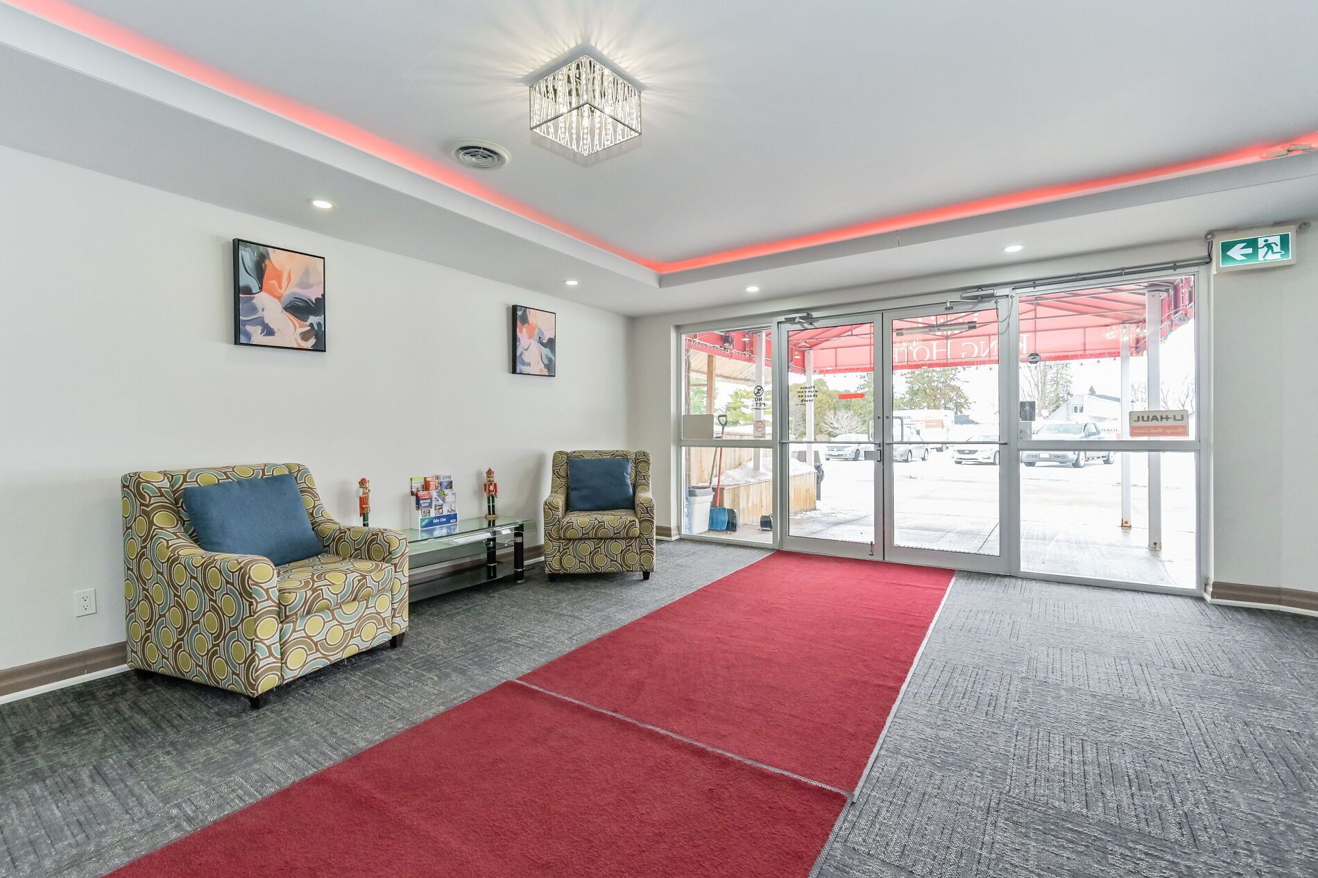 Zona de recepción con dos sillones estampados, una alfombra roja y una puerta de vidrio que da al exterior.