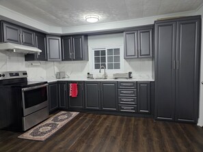 A kitchen with dark cabinets, a stainless steel stove, a window, and a patterned rug.