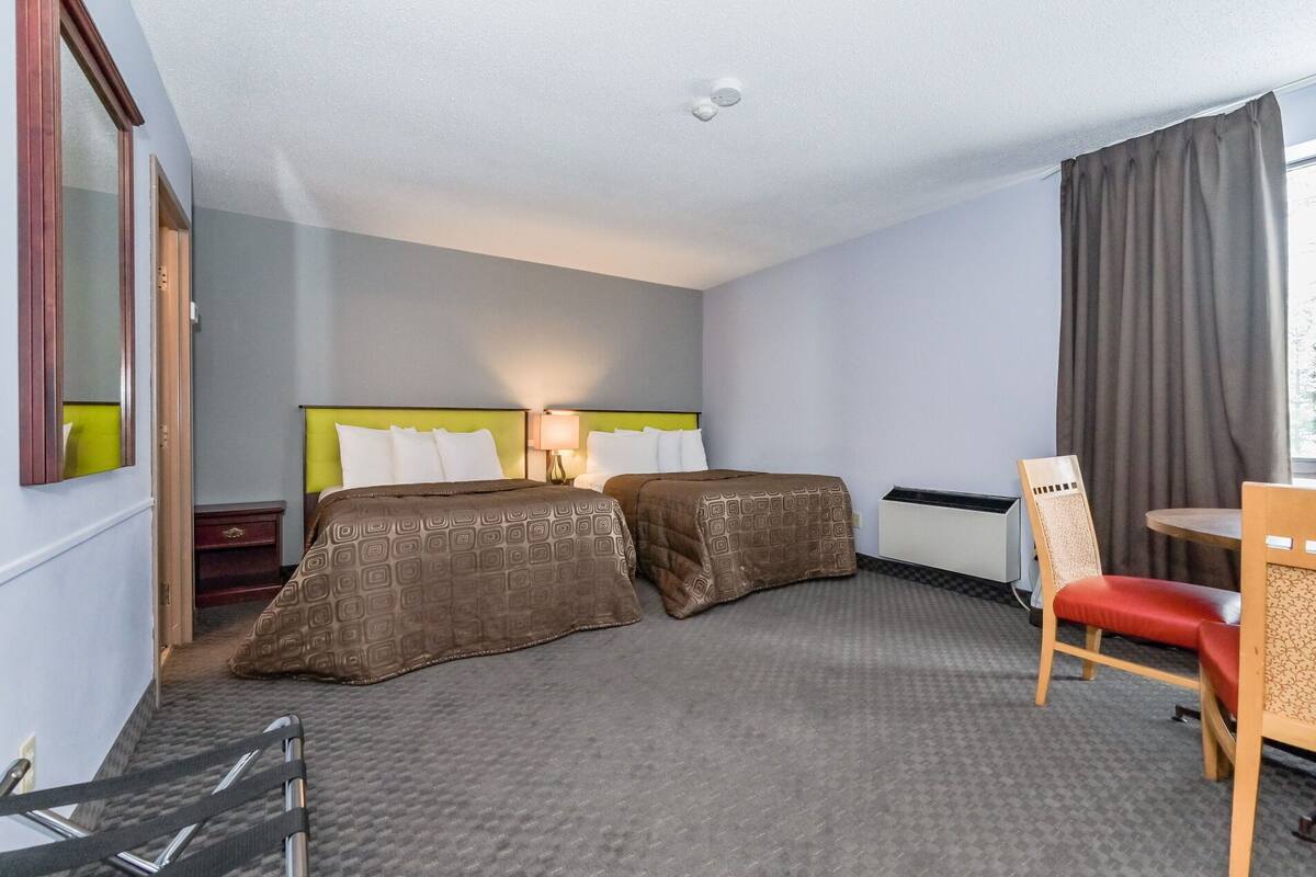 A hotel room with two beds, a desk, a chair, and a window with curtains.