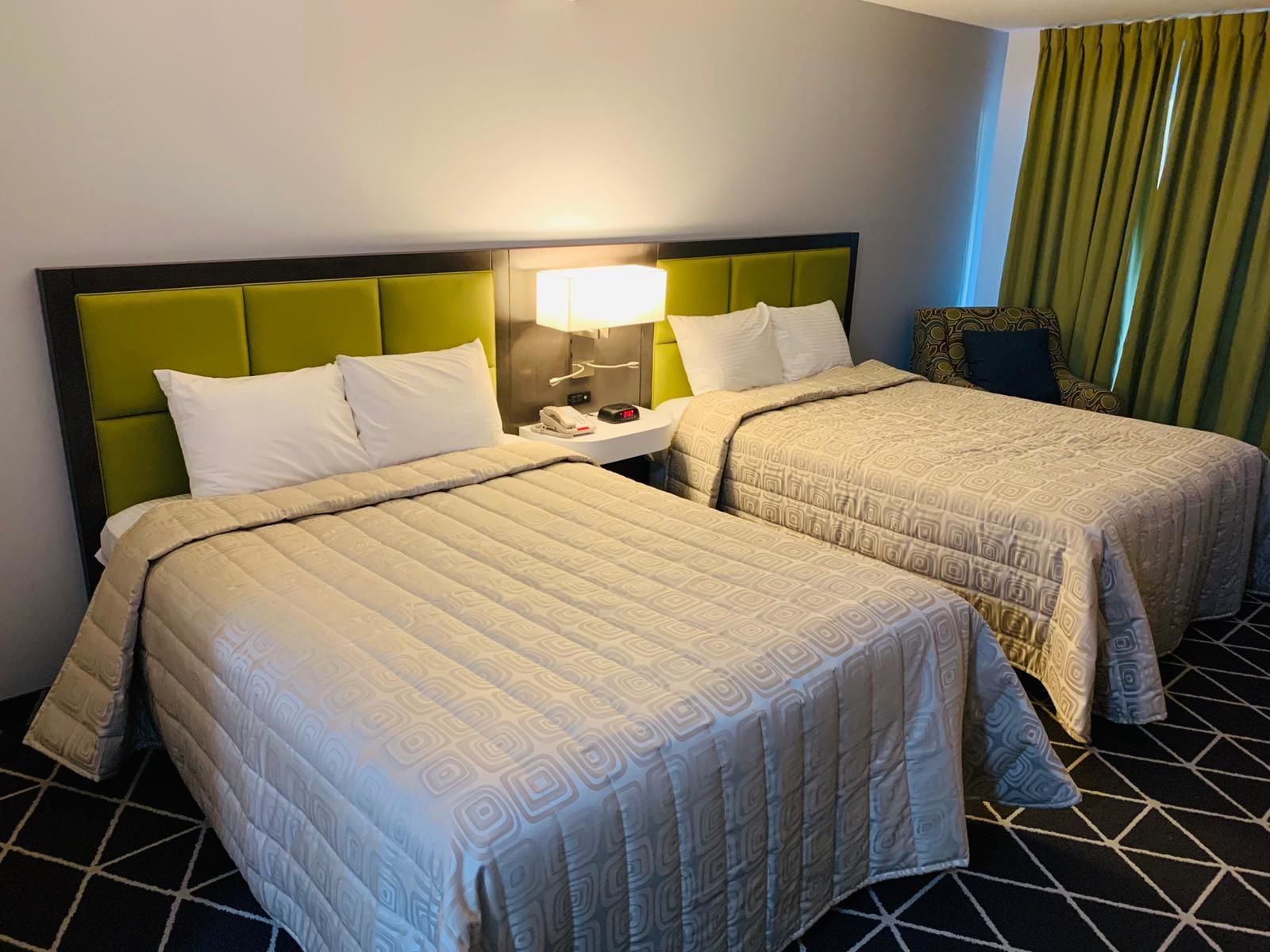 A hotel room with two beds, a nightstand, a lamp, and a patterned floor.