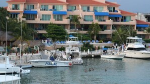 Uma marina com barcos atracados, um edifício com varandas e palmeiras.