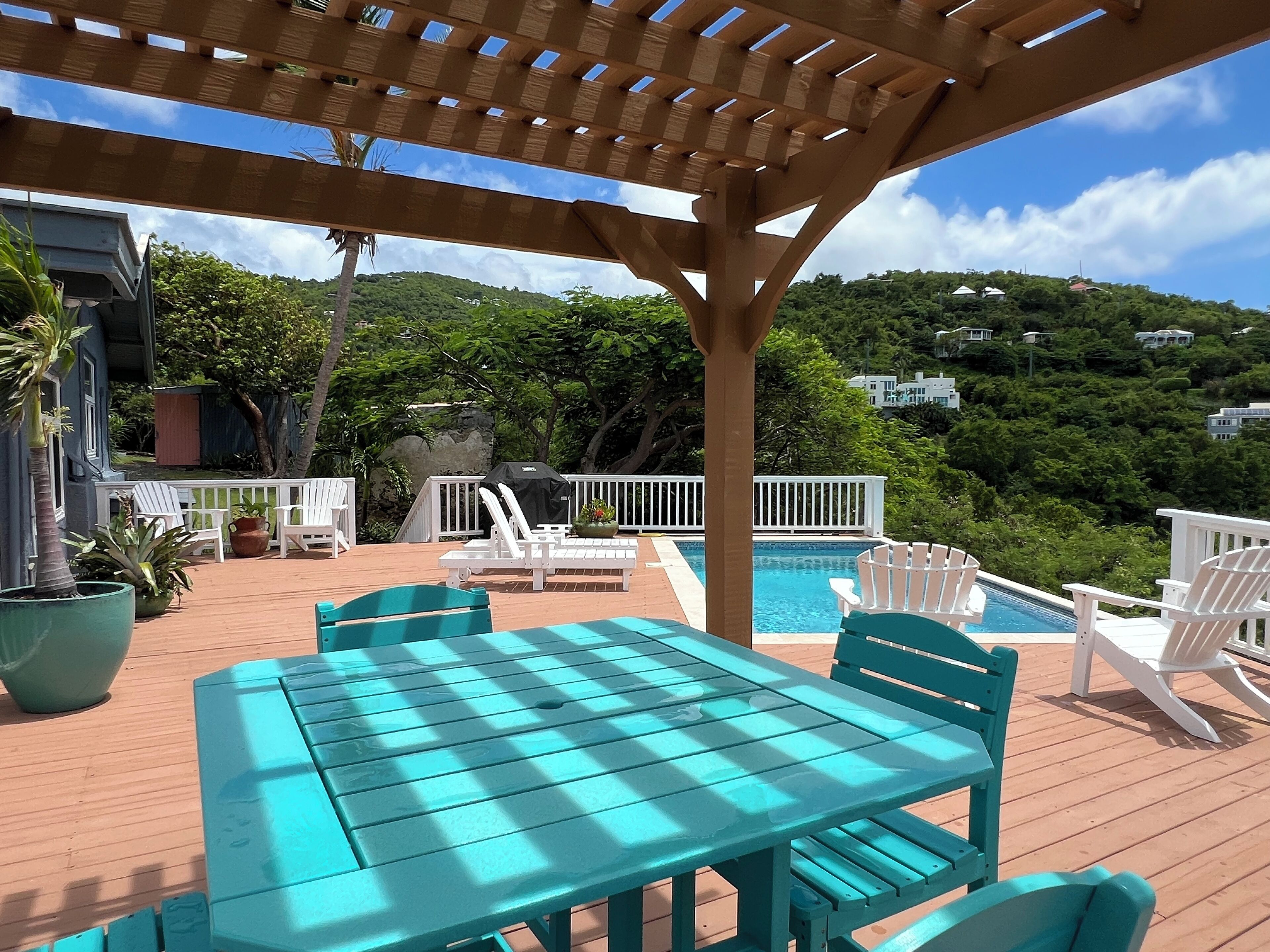 Une terrasse en bois avec une piscine, des chaises blanches et une table.