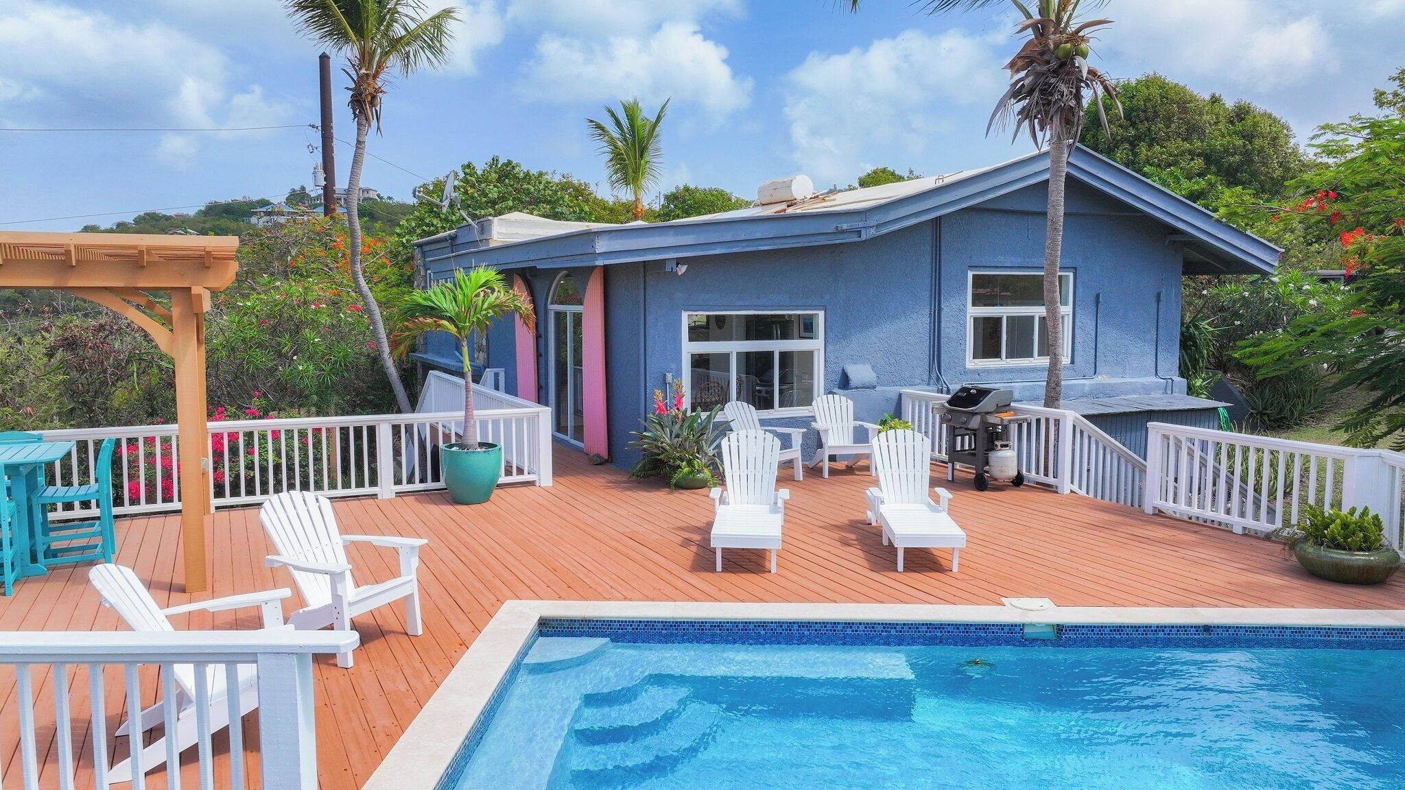 A blue house with a wooden deck, a swimming pool, and outdoor seating.