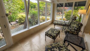 A conservatory with a view of a garden, featuring a seating area with floral-patterned chairs and a small table.