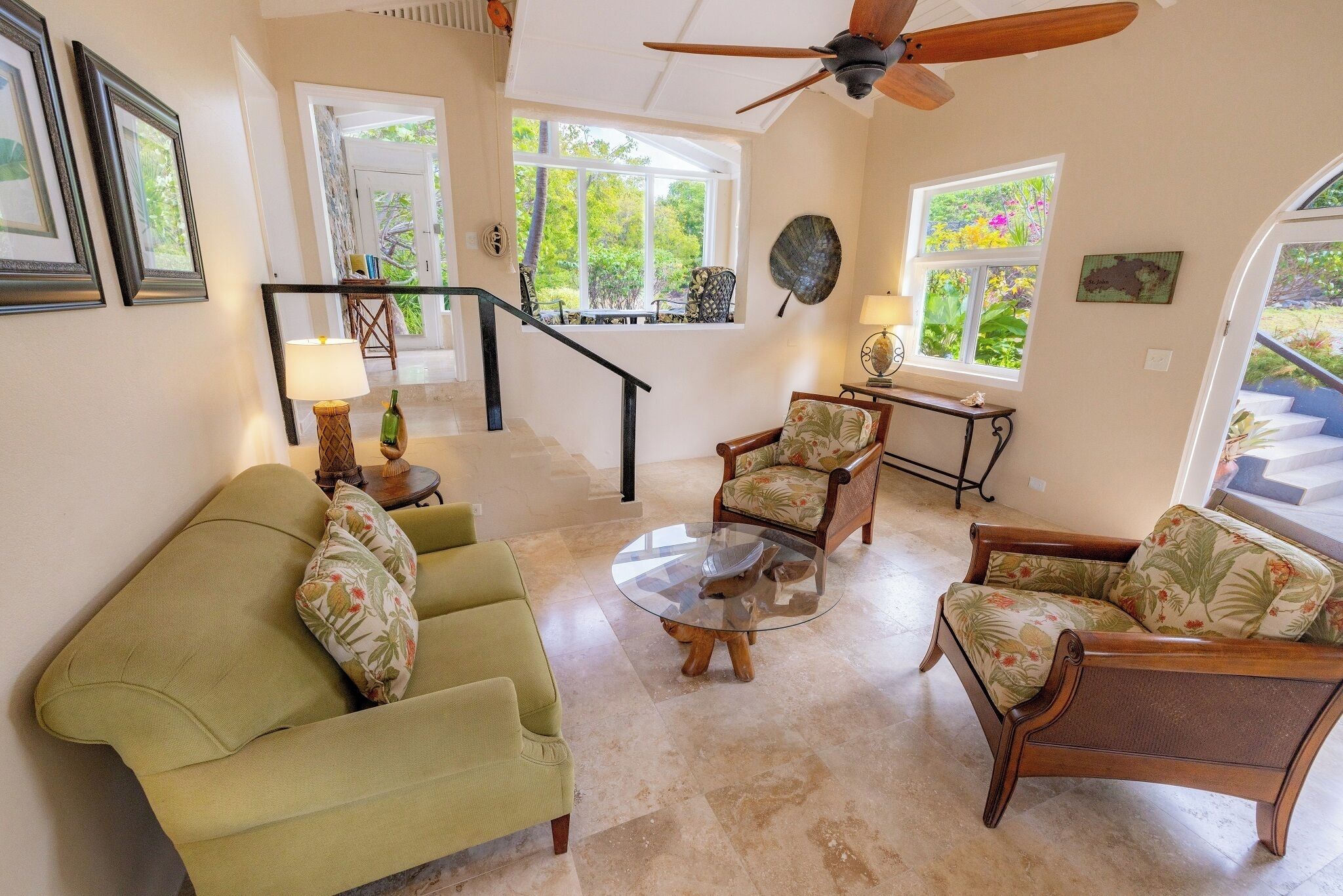A spacious living room with a green sofa, two armchairs, a coffee table, and a staircase leading to another level.