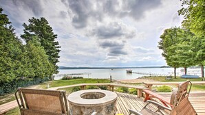 A deck with wicker chairs and a fire pit, overlooking a lake and dock.
