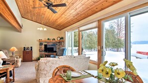 A cozy living room with a fireplace, a dining table set with plates and a vase of flowers, and a large window offering a view of the outdoors.
