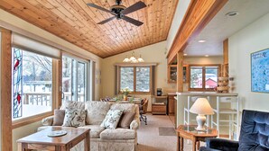 A cozy living room with a wooden ceiling, a sofa, a dining table, and a lamp.