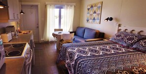 Ein gemütlicher Raum mit Bett, einer Couch, einem kleinen Tisch, einer Küchenzeile mit Herd und einem Fenster mit Vorhängen.