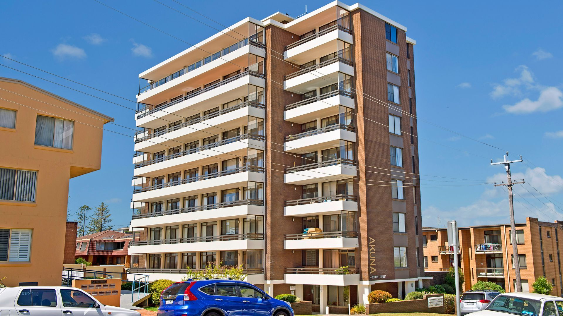 Un immeuble résidentiel à plusieurs étages, doté de balcons, d’un espace de stationnement et surplombant un ciel dégagé.