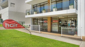 Un bâtiment moderne avec une façade vitrée, un balcon bien visible et une banderole rouge sur laquelle est écrit le mot « cheveux », le tout donnant sur le trottoir.