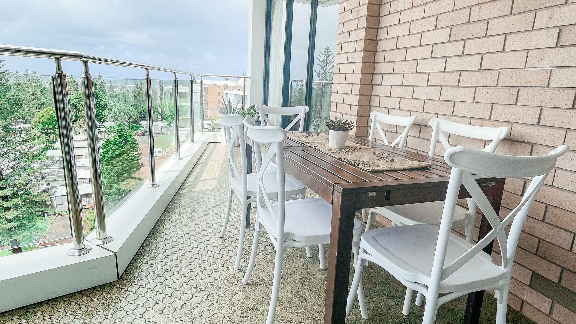 Un balcón con mesa y sillas, vistas a la vegetación y un muro de ladrillo.