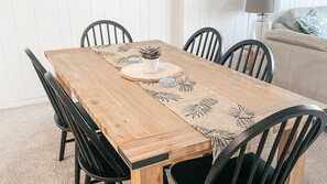 Une table de salle à manger rectangulaire en bois, surmontée d’un set de table en fibres tressées, entourée de chaises noires et agrémentée d’une petite plante en pot.