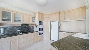 Une cuisine avec des meubles de couleur bois clair, un plan de travail noir, un four encastré, un four à micro-ondes et un réfrigérateur.
