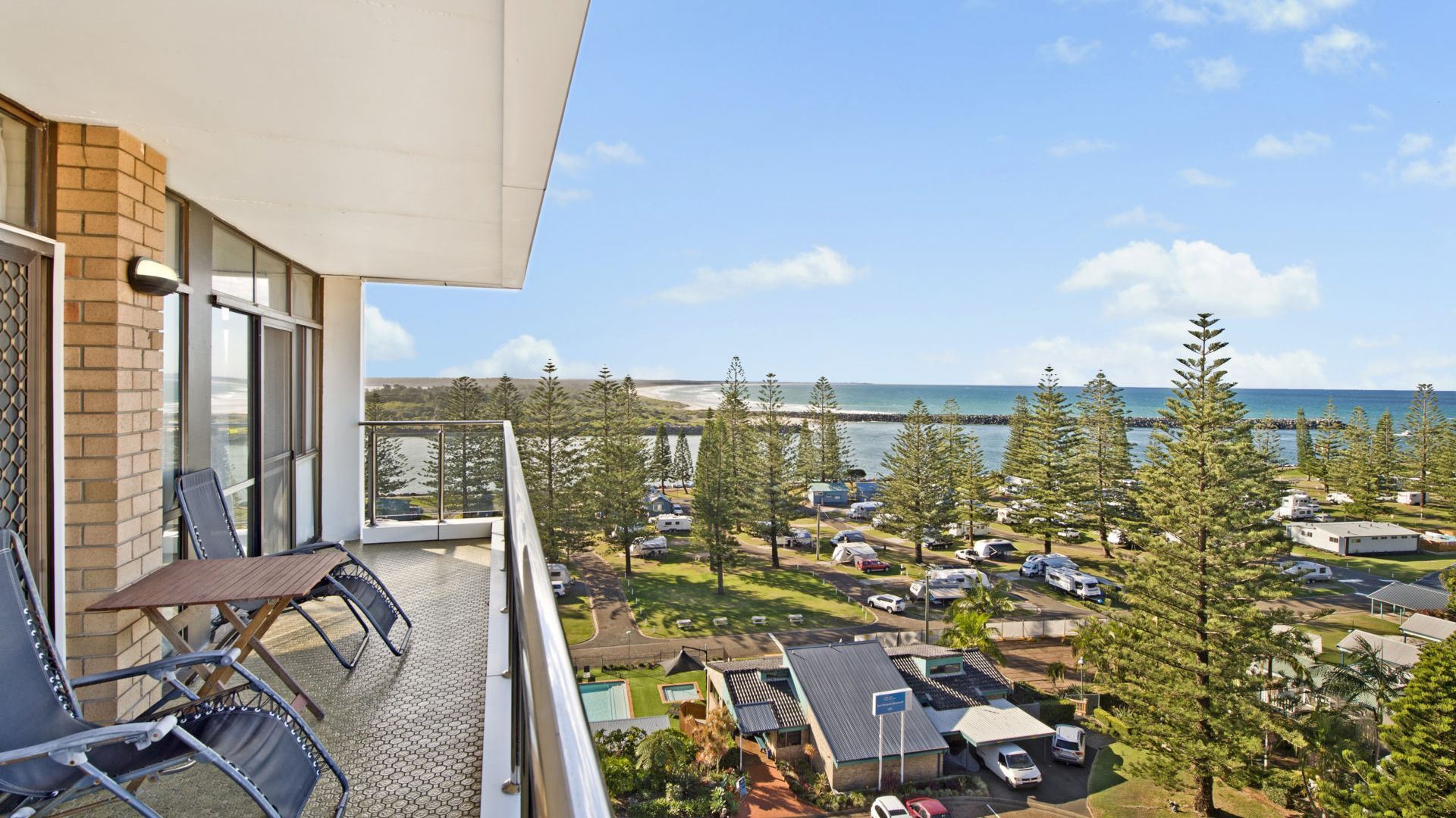 A balcony with a view of a beach and parked vehicles.