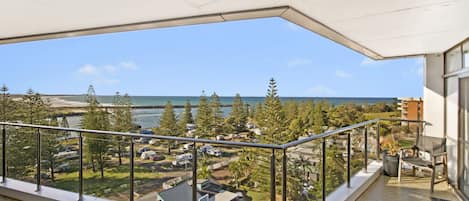 Ein Balkon mit Blick auf Strand und Meer, mit Metallgeländern und blauem Himmel.