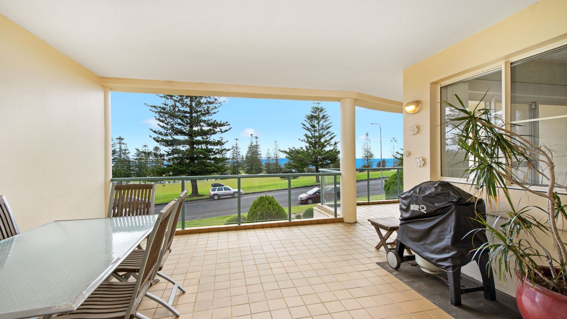 A balcony with a dining table and chairs, a grill, and a potted plant.