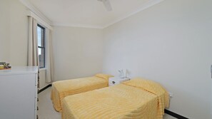 A simple, clean room with two beds, a desk, and a window.