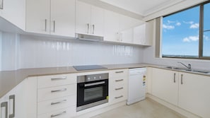 Eine moderne Küche mit weißen Schränken, einem eingebauten Backofen, einem Geschirrspüler und einem Fenster mit Blick zum Himmel.