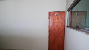 A room with a wooden door marked with the number 08, a tiled floor, and a window with a view of another building. - Hotel Reobot (Garanhuns)
