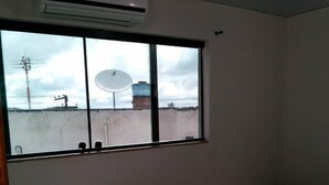 A room with two single beds, a window with a view of the outside, and an air conditioning unit above the window. - Hotel Reobot (Garanhuns)