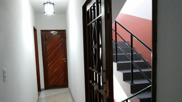 A hallway with a tiled floor, a wooden door with a number, and a staircase with a metal railing. - Hotel Reobot (Garanhuns)