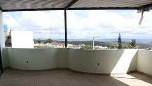 A covered balcony with a view of a residential area and distant hills. - Hotel Reobot (Garanhuns)