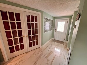A hallway with a white door, a glass door with a grid pattern, and a tiled floor.