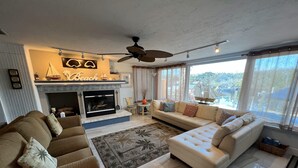 A living room with a fireplace, two sofas, a coffee table, and a large window with a view. - 3BR Waterfront Oasis w/ Private Solar Heated Pool and Spacious Deck (Holiday)