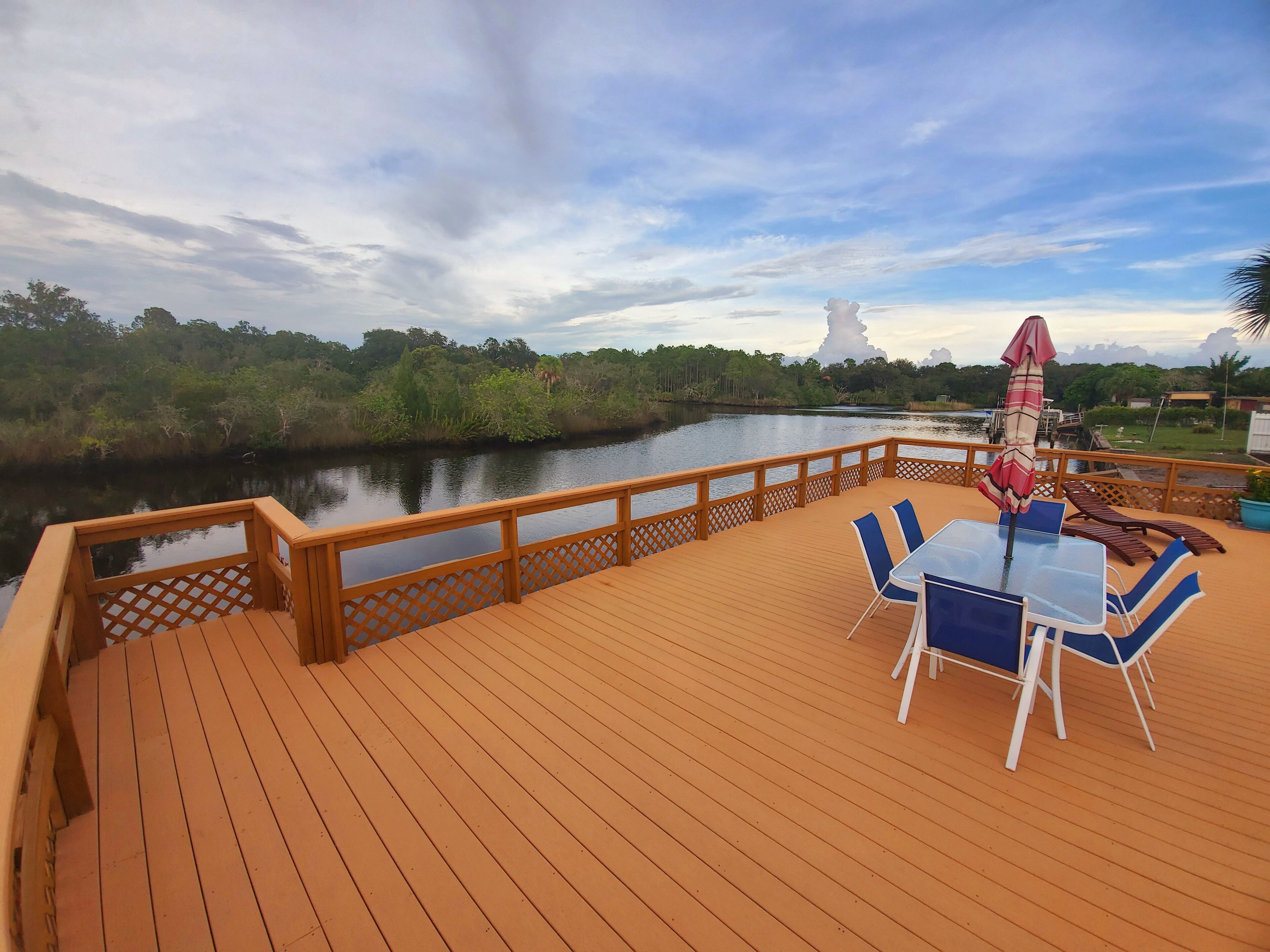 Une terrasse en bois avec une table et des chaises, donnant sur une rivière paisible et une végétation luxuriante.