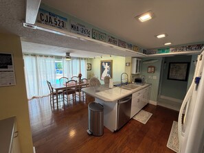 A kitchen with a central island, a dining area with chairs, a trash can, and a refrigerator. - 3BR Waterfront Oasis w/ Private Solar Heated Pool and Spacious Deck (Holiday)