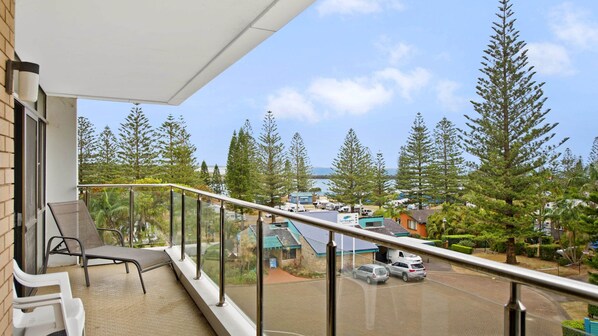 A balcony with a glass railing overlooking a parking area and a view of trees and buildings.