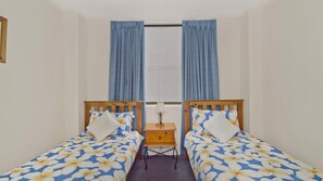 A room with two single beds, a small wooden nightstand, and a window with curtains.