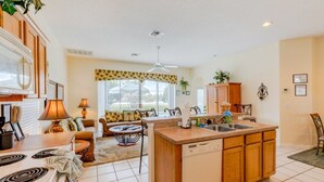 A modern kitchen with a central island, a dining area with a sofa and chairs, and a view of the outdoors through large windows.