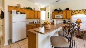 A kitchen with wooden cabinets, a white refrigerator, a microwave, a stove, and a dining area with a table and chairs.
